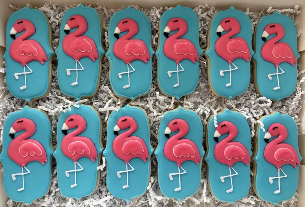 A dozen pink flamingo cookies on turquoise plaques, hand-piped by Kristin