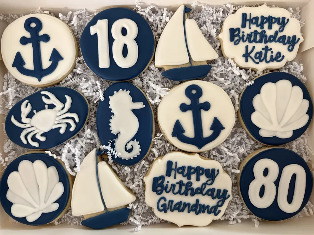 Navy and white nautical birthday cookies with anchors, sailboats, a crab and seashells