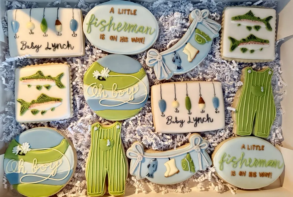 Green and blue fishing-themed baby shower cookies with fish, overalls and lures